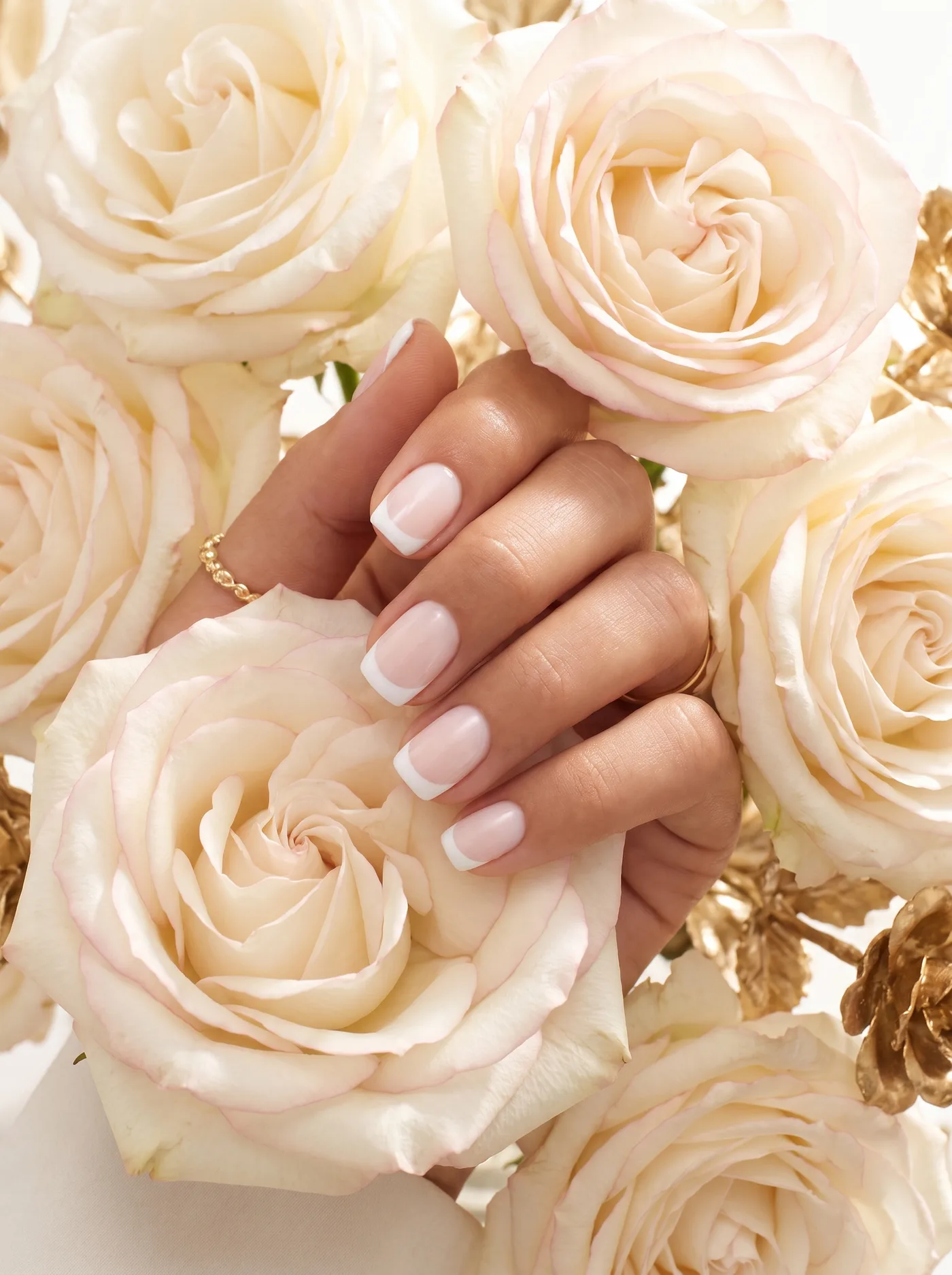 Classic short French manicure resting on ivory-white and gilded gold roses.